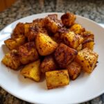 A close-up of golden, roasted Mexican Potatoes seasoned with chili powder, served on a white plate.