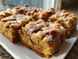 Close-up of several squares of moist apple brownies topped with pecans and a vanilla glaze.