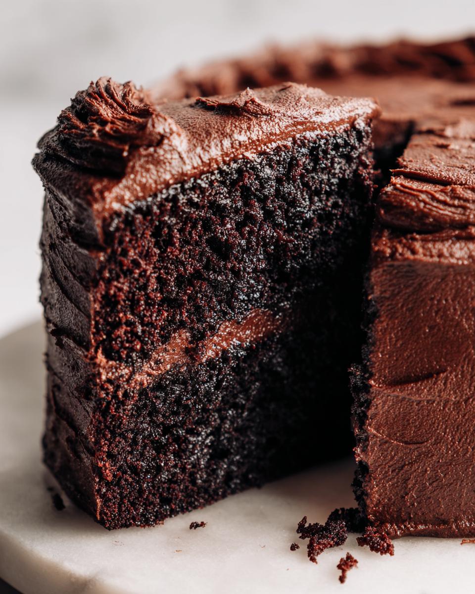 Close-up of a rich, dark slice cut from a homemade chocolate cake showing moist crumb and thick chocolate frosting.
