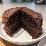 A rich, dark slice cut from a homemade chocolate cake covered in thick chocolate frosting.