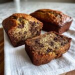 Close-up of moist mini banana bread loaves, one sliced to show chocolate chips throughout the crumb.