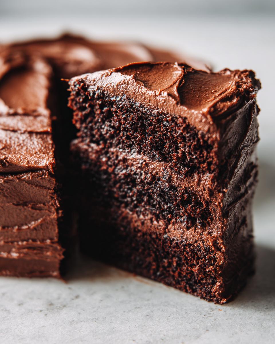 Close-up of a moist slice of homemade chocolate cake layered with thick chocolate frosting.
