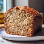 A close-up, cross-section view of a moist loaf of sugar free banana bread with visible walnuts on a white plate.