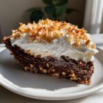 A decadent slice of no-bake german chocolate pie featuring a thick chocolate layer, whipped cream, and toasted coconut.