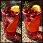 Two glasses of vibrant non-alcoholic christmas punch garnished with fresh cranberries, an orange slice, and rosemary sprigs.