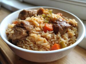 Close-up of a white bowl filled with one pot chicken and rice, mixed with chunks of meat, carrots, and celery.