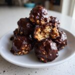 A stack of no-bake pecan pie balls coated in dark chocolate, with one bitten open showing the nutty interior.