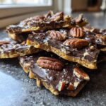 A stack of broken pieces of rich Pecan Pie Bark featuring a toffee base, dark chocolate topping, and whole pecans.