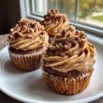 Three delicious pecan pie cupcakes topped with thick, swirled brown sugar frosting and chopped pecans, sitting on a white plate.