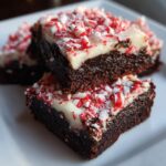 Two rich, dark chocolate peppermint brownies stacked, topped with white frosting and crushed candy canes.