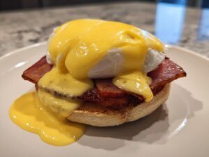 Close-up of a delicious Eggs Benedict featuring a poached egg, bacon, and rich hollandaise sauce dripping onto an English muffin.