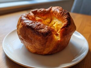 A single, large, golden-brown Yorkshire pudding with a dramatic rise sitting on a white plate.