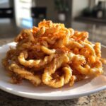 A large pile of golden brown, crispy, curly cheese straws stacked high on a white plate.