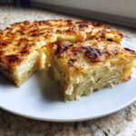 A thick slice of perfectly baked potatoes au gratin showing layered potatoes and creamy sauce, served on a white plate.