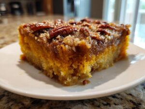 Close-up of a moist square slice of pumpkin pecan cobbler, featuring a rich orange base and a sticky pecan topping.