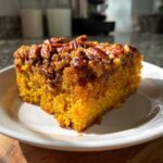 A close-up, sunlit slice of moist pumpkin pecan cobbler on a white plate.