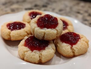 A stack of five buttery raspberry thumbprint cookies with bright red jam centers on a white plate.