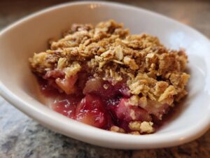 Close-up of a warm serving of rhubarb crisp showing bubbly fruit filling and golden oat topping.