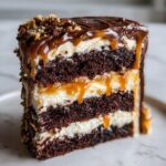 Close-up of a rich Capricorn cake slice showing three layers of dark chocolate cake, white frosting, and dripping caramel sauce.