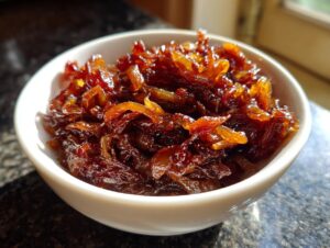 A close-up of deeply browned, glossy caramelized onions filling a small white bowl.