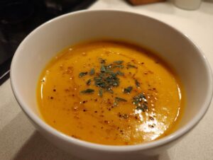 A close-up of creamy roasted butternut squash soup, garnished with herbs and oil droplets.