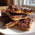 A stack of homemade saltine cracker toffee bars with a thick chocolate top layer resting on a white plate.