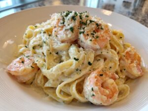 Close-up of fettuccine pasta coated in creamy sauce, topped with shrimp alfredo, grated parmesan, and parsley.