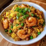 A close-up of a white bowl filled with flavorful shrimp fried rice recipe, featuring large shrimp, peas, egg, and green onions.