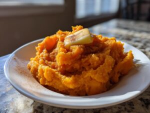 A serving of bright orange, fluffy mashed sweet potatoes topped with melting butter and cinnamon.