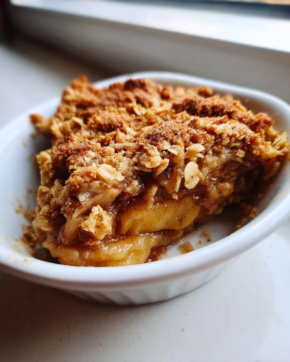 Close-up of a warm, bubbling single serving apple crisp with an oat topping in a white ramekin.