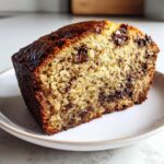 Close-up of a moist slice of chocolate chip banana bread with a dark, caramelized crust.