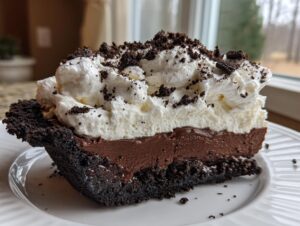 A generous slice of rich Oreo pie showing a dark crust, chocolate filling, and whipped cream topping with cookie crumbles.