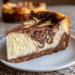 A close-up of a rich slice of snickerdoodle cheesecake showing the creamy white filling swirled with cinnamon topping.