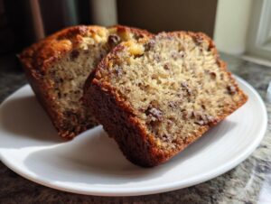 Two moist slices of homemade banana bread recipe displayed on a white plate, showing chocolate chips.
