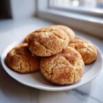 A stack of freshly baked, soft snickerdoodle cookies coated in cinnamon sugar on a white plate.