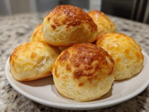 A stack of freshly baked, golden-brown sourdough discard rolls piled on a white plate.