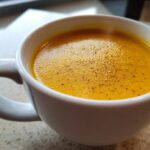Close-up of creamy, bright orange squash soup topped with black pepper in a white mug.