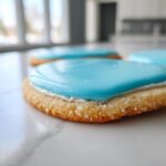 Close-up of a sugar cookie topped with white and bright blue sugar cookie icing that hardens, sitting on marble.