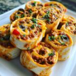 A pile of freshly baked taco pinwheels filled with seasoned ground beef, melted cheese, and garnished with cilantro.