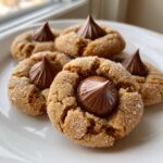 Four freshly baked kiss cookies, rolled in sugar, with a chocolate kiss pressed into the center.
