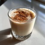 A creamy glass of homemade coquito topped generously with ground cinnamon.