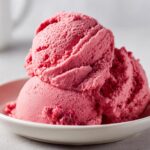 Close-up of two scoops of vibrant pink strawberry ice cream in a white bowl.