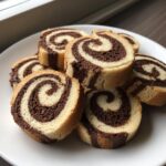Several slices of two-tone pinwheel cookies showing a perfect vanilla and chocolate swirl pattern, piled on a white plate.