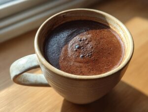 Close-up of a rich, dark french hot chocolate with a slight foam topping in a rustic ceramic mug.