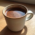 Close-up of rich, dark french hot chocolate with a slight foam layer in a rustic ceramic mug.