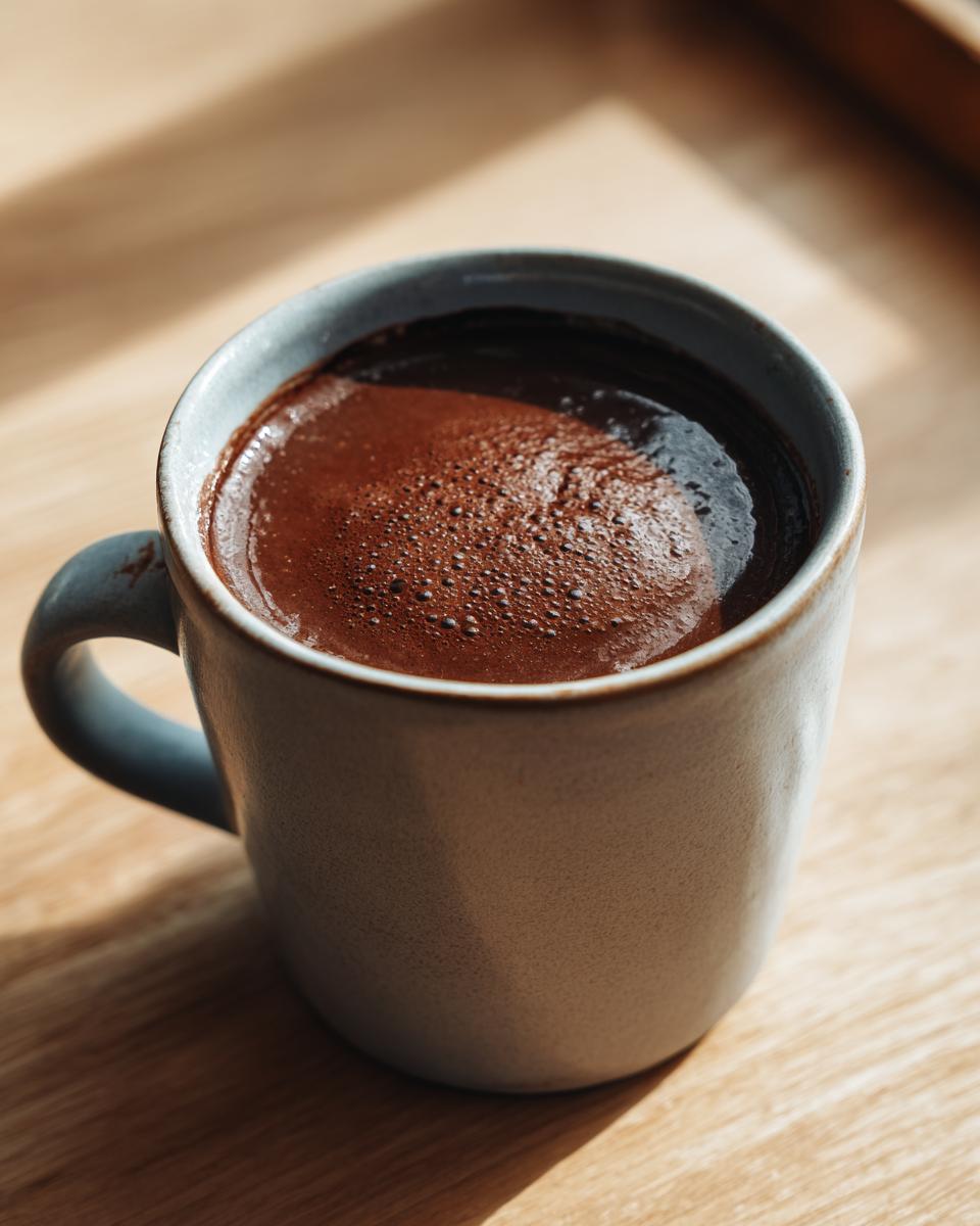 Close-up of rich, dark french hot chocolate with small bubbles on the surface in a light blue ceramic mug.