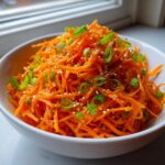 Close-up of a vibrant raw carrot salad, shredded and tossed with sesame seeds and green onions.
