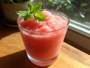 A frosty glass filled with a bright pink watermelon smoothie, topped with fresh mint leaves.