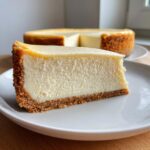 A thick, creamy slice of white chocolate cheesecake with a graham cracker crust on a white plate.